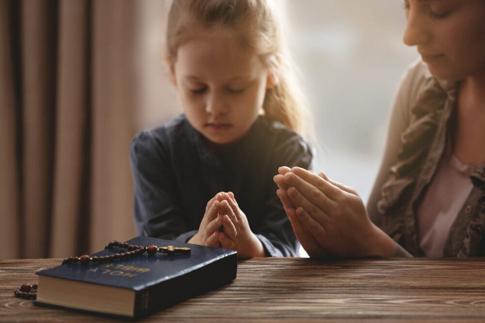 Religious Christian girl praying with her mother indoors