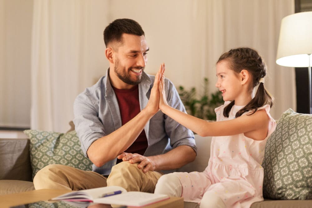 Father and daughter smiling while giving a high-five on a cozy couch