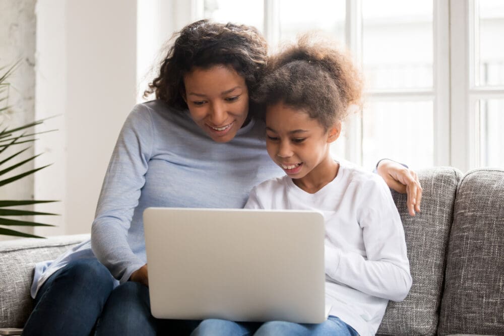Happy African American attractive mother and little preschooler daughter using laptop